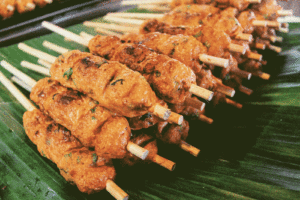 Barbecued satay chicken on skewers resting on bamboo leaves
