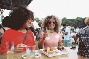 Two women eating and drinking at The Great Ethnic Food Festival